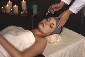 A modern med spa treatment room in Florida with soft natural lighting. A woman receiving a non-invasive aesthetic treatment like RF microneedling or Hydrafacial, looking relaxed and confident. Include subtle high-tech skincare equipment in the background, warm-toned interior, clean spa aesthetic, and tropical greenery outside a window to reflect the Florida vibe. Text overlay: “Advanced Aesthetics in Florida – River Med Spa