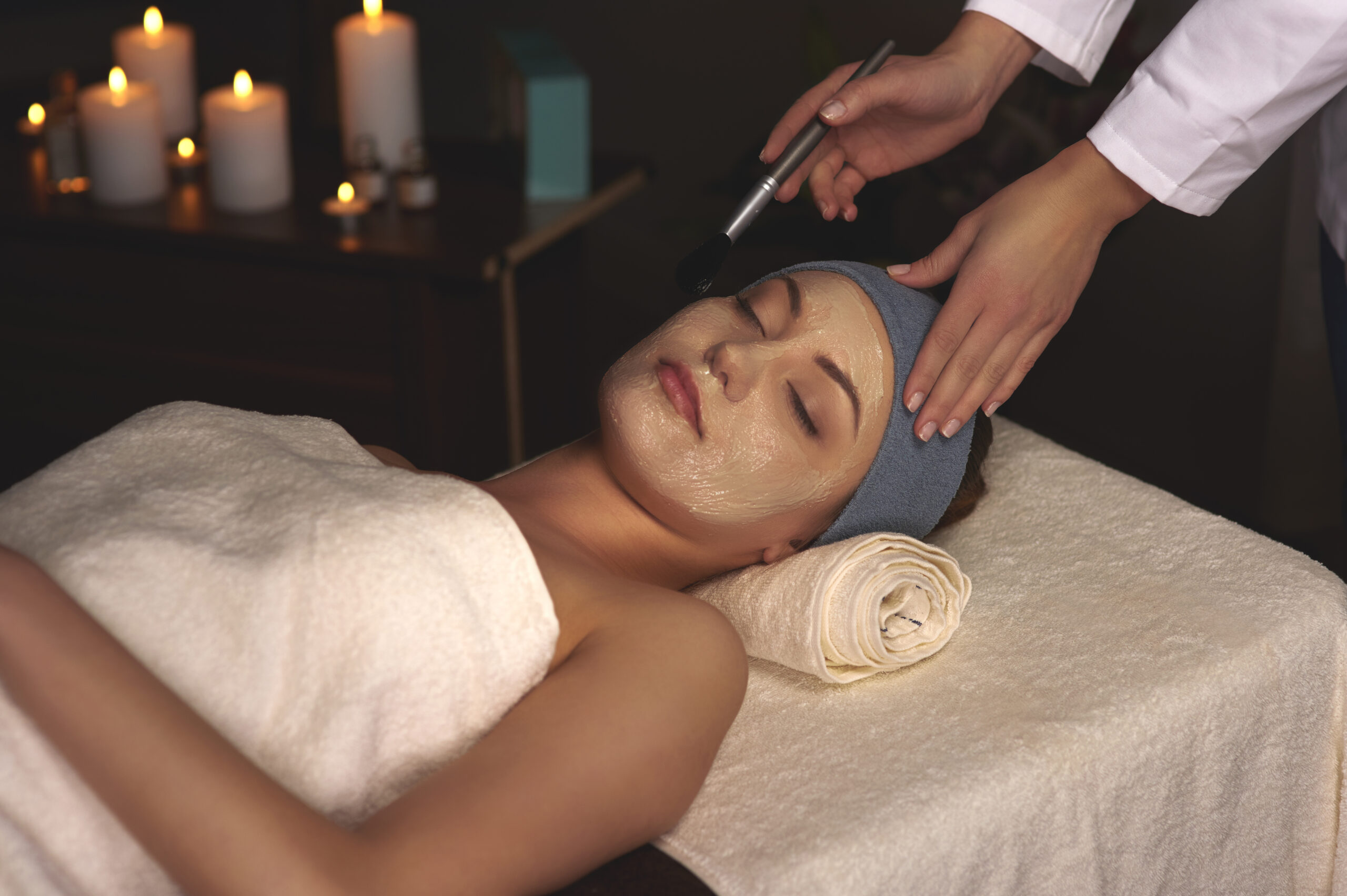 A modern med spa treatment room in Florida with soft natural lighting. A woman receiving a non-invasive aesthetic treatment like RF microneedling or Hydrafacial, looking relaxed and confident. Include subtle high-tech skincare equipment in the background, warm-toned interior, clean spa aesthetic, and tropical greenery outside a window to reflect the Florida vibe. Text overlay: “Advanced Aesthetics in Florida – River Med Spa